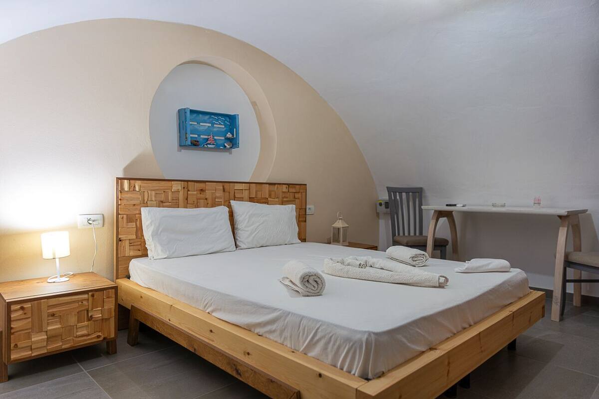 A single bedroom with a wooden bed, a nightstand, a desk, and a chair.