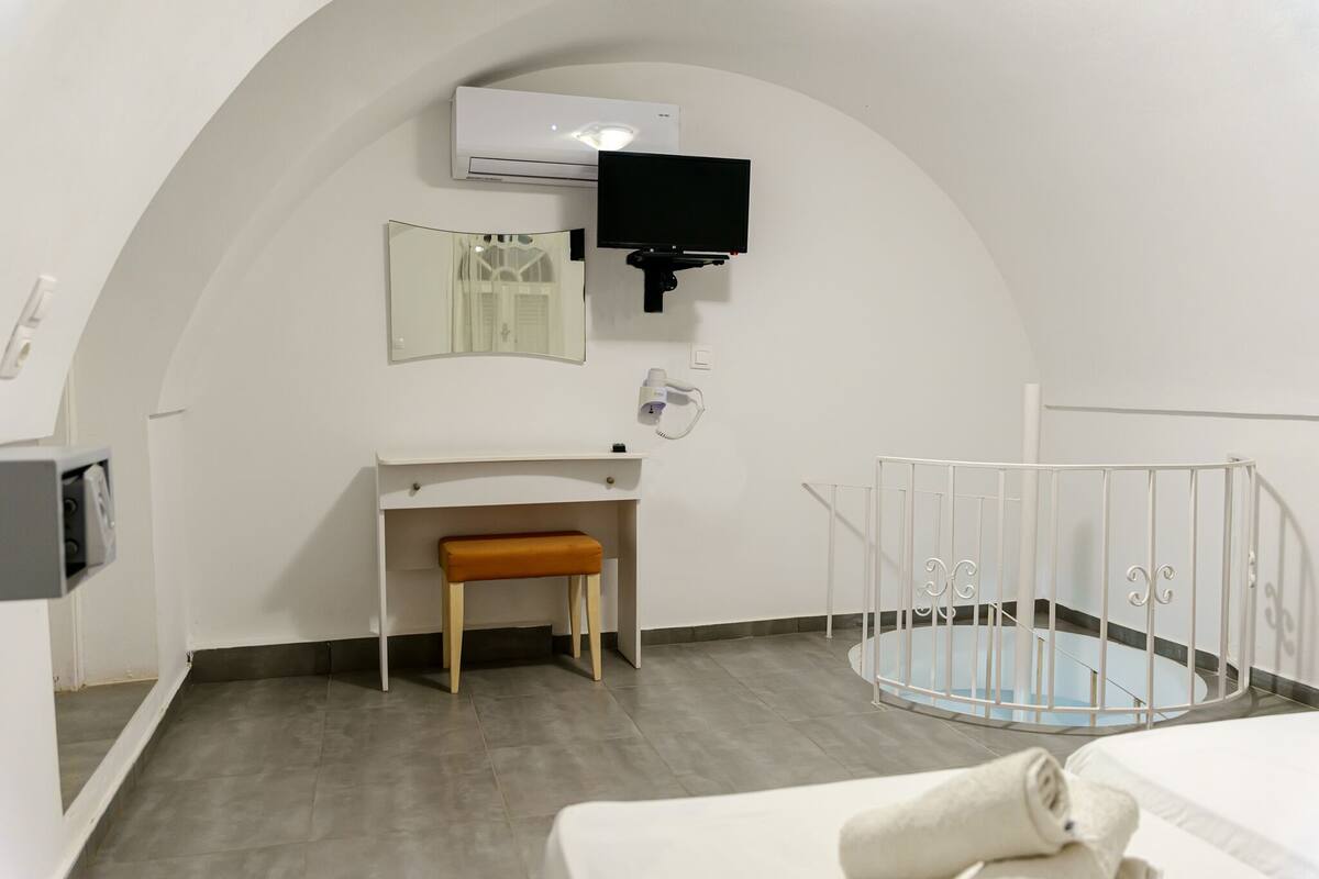 A modern room with a white curved wall, a small wooden bench, a white crib, a flat-screen TV mounted on the wall, and a white air conditioning unit.