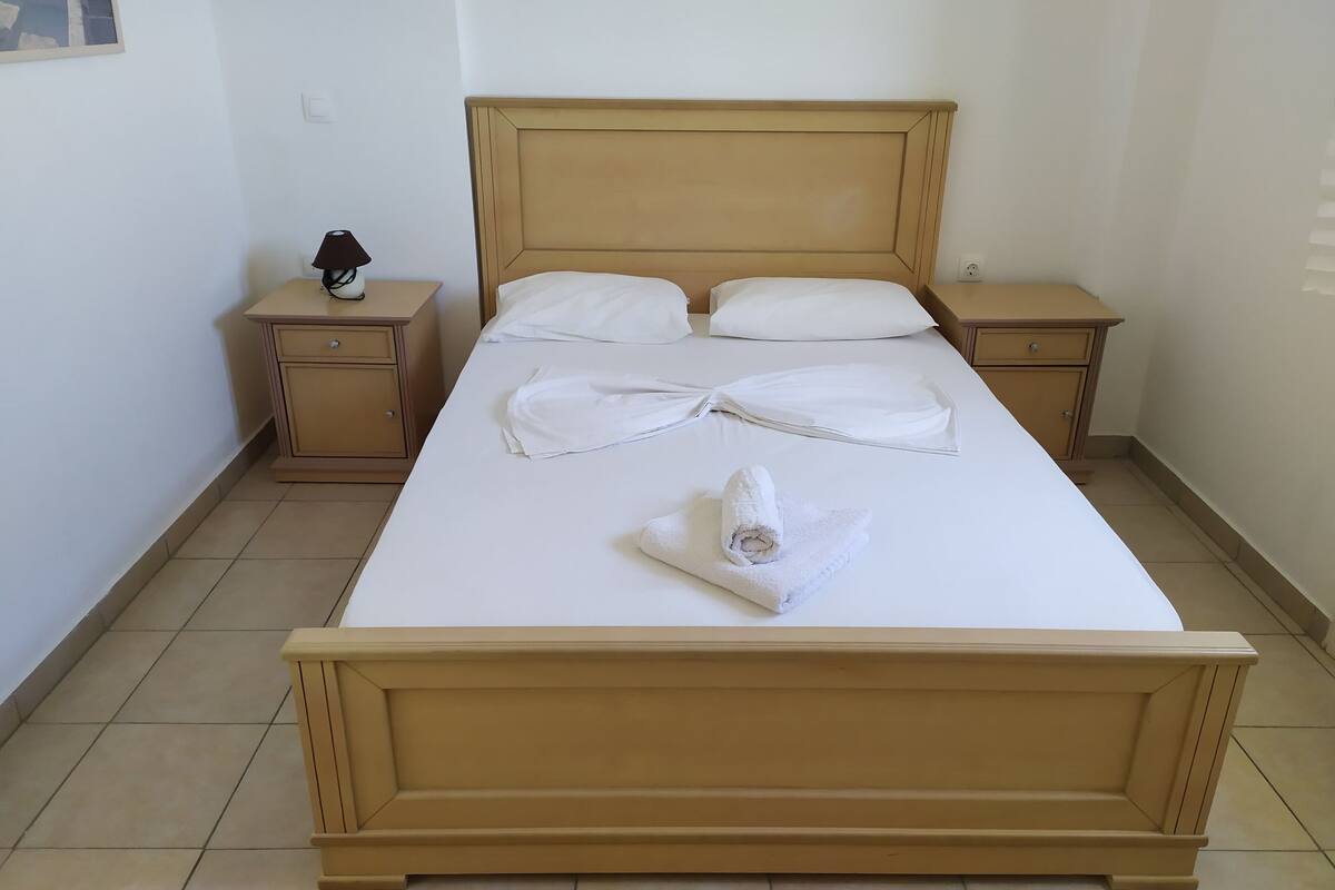 A neatly made bed with white linens and towels, two bedside tables, and a wall-mounted light fixture.