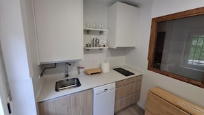 A compact kitchen with white cabinets, a dishwasher, a sink, and a window with a view of greenery.