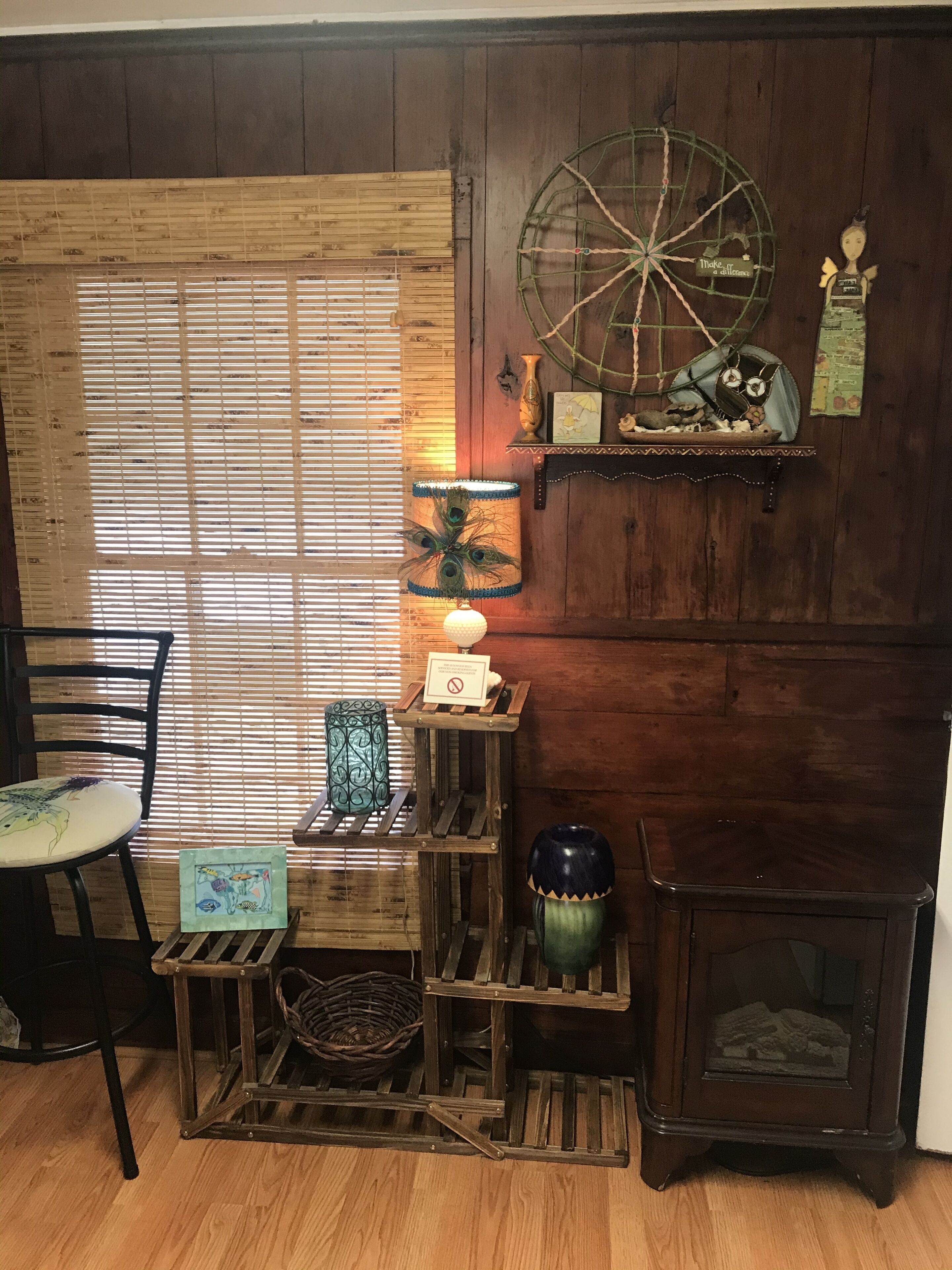 Ein gemütliches Zimmer mit Holzboden, einem Fenster mit Jalousien, einer rustikalen Holzablage mit Dekoration, einem kleinen Tisch mit Stuhl und einem Herd im Vintage-Stil.