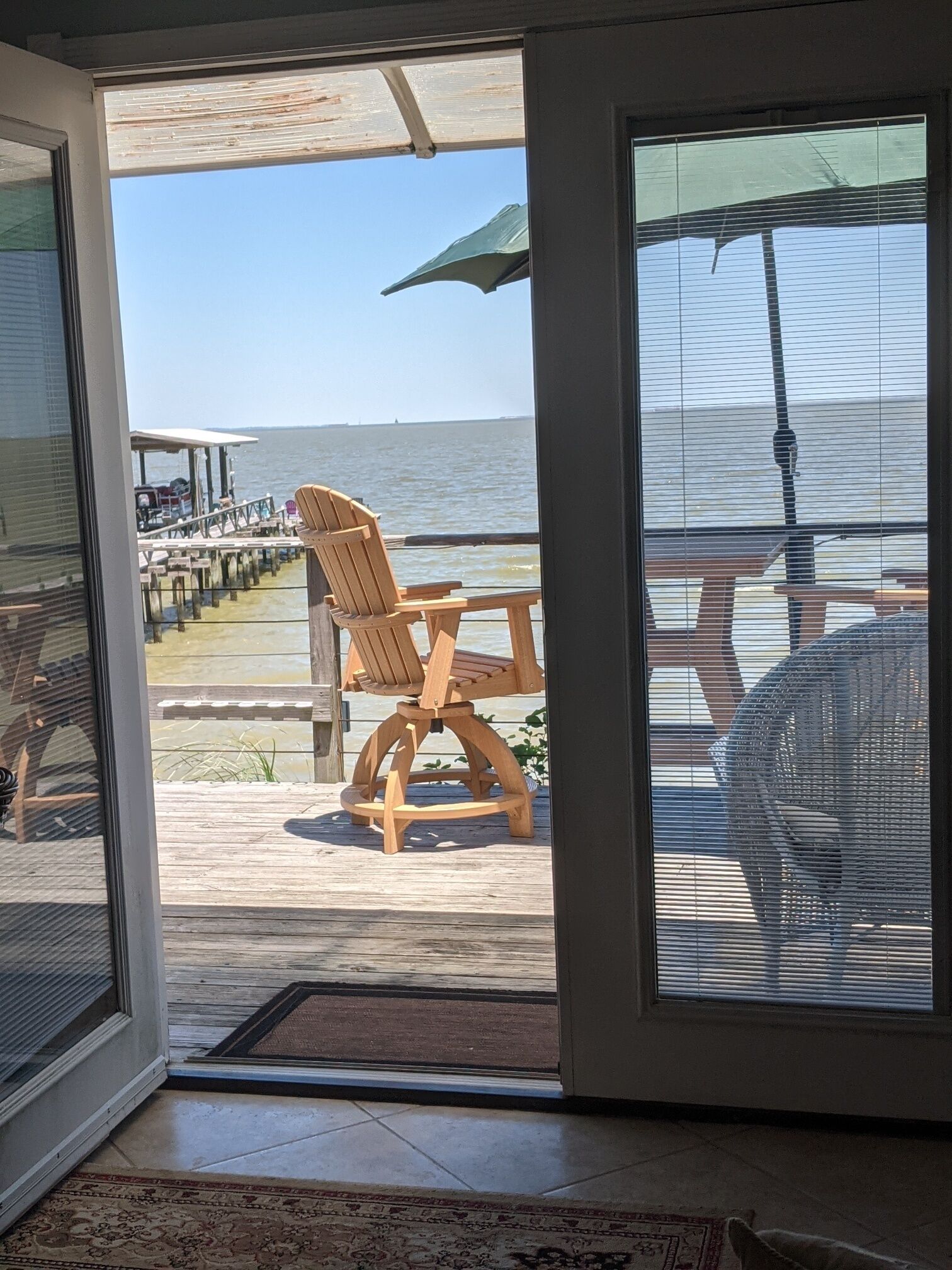 Eine Holzterrasse mit Stuhl und Sonnenschirm mit Blick auf einen Steg und das Meer.