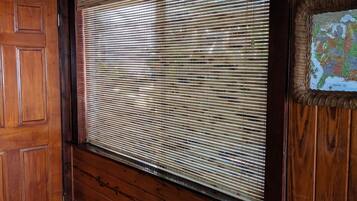 Una habitación con paneles de madera, una ventana grande cubierta por persianas, una puerta y una lámpara fijada a la pared.