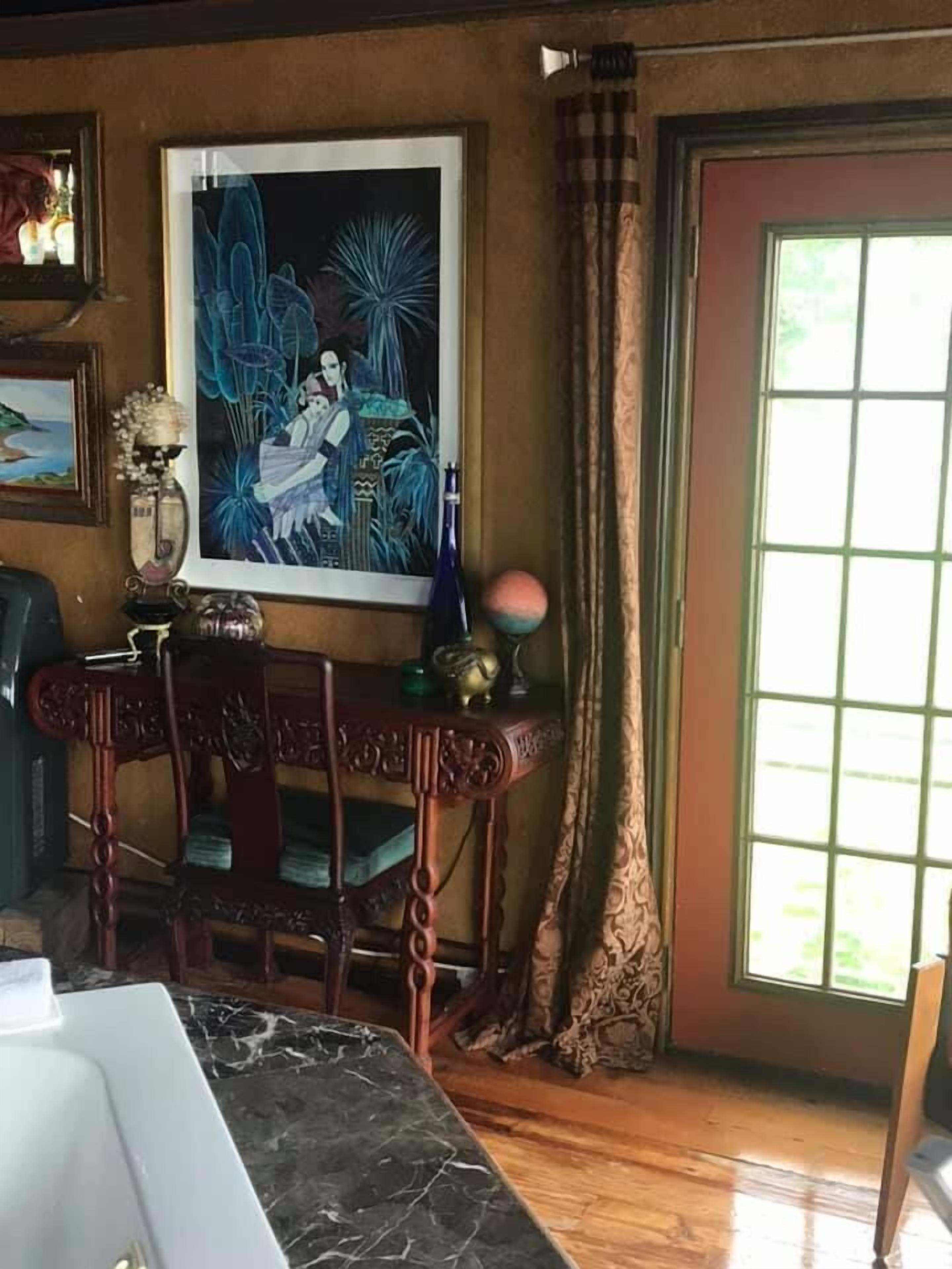 A dining area with a marble table, a wooden chair, a framed painting, and a window with curtains.