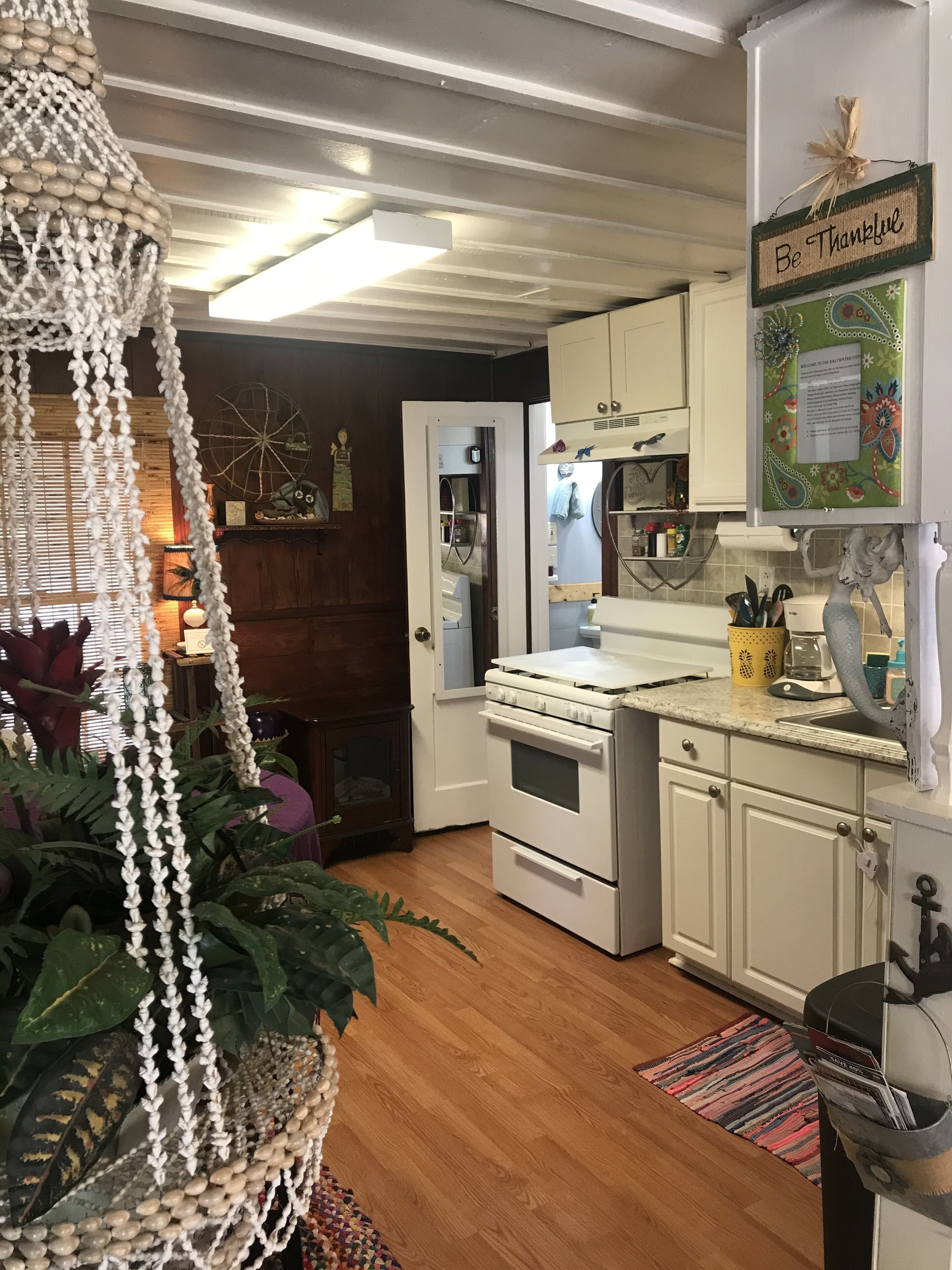 A kitchen with white cabinets, a white stove, and a refrigerator. There is a 'Be Thankful' sign on the wall.