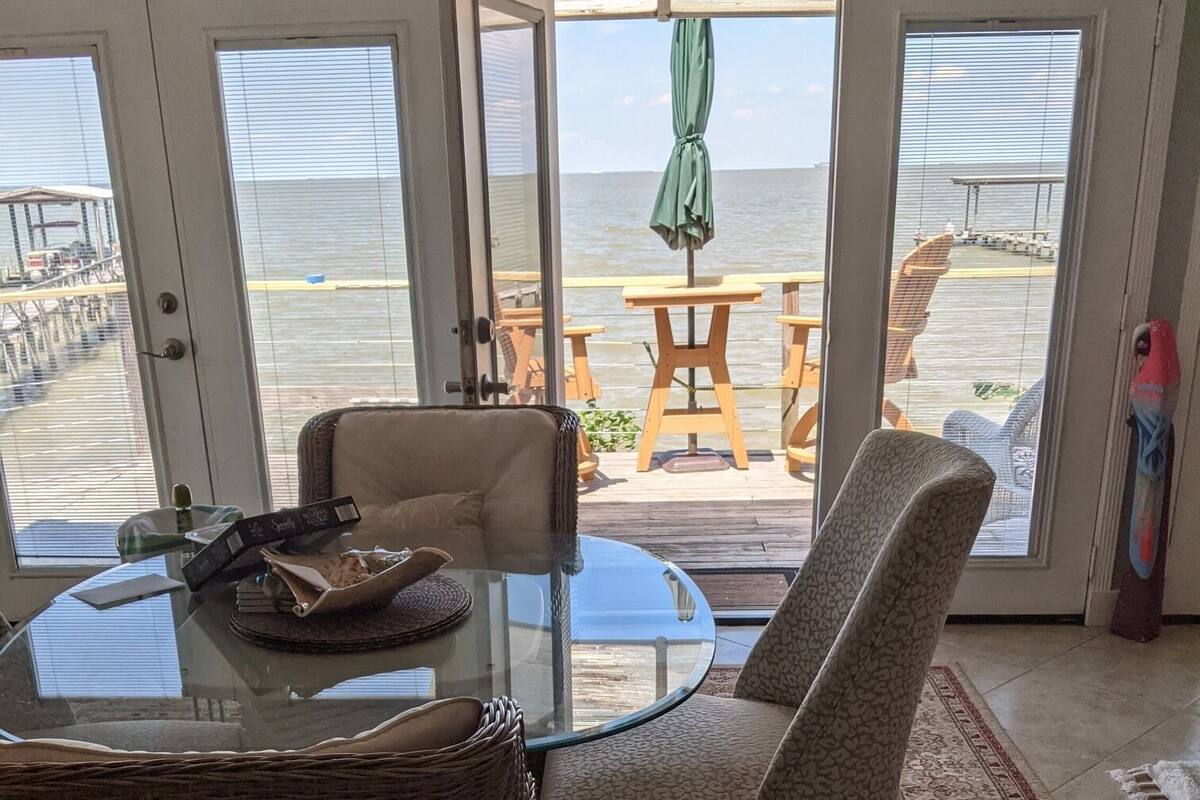 Een eetgedeelte met een glazen tafel, rieten stoelen en uitzicht op de oceaan door grote glazen deuren.