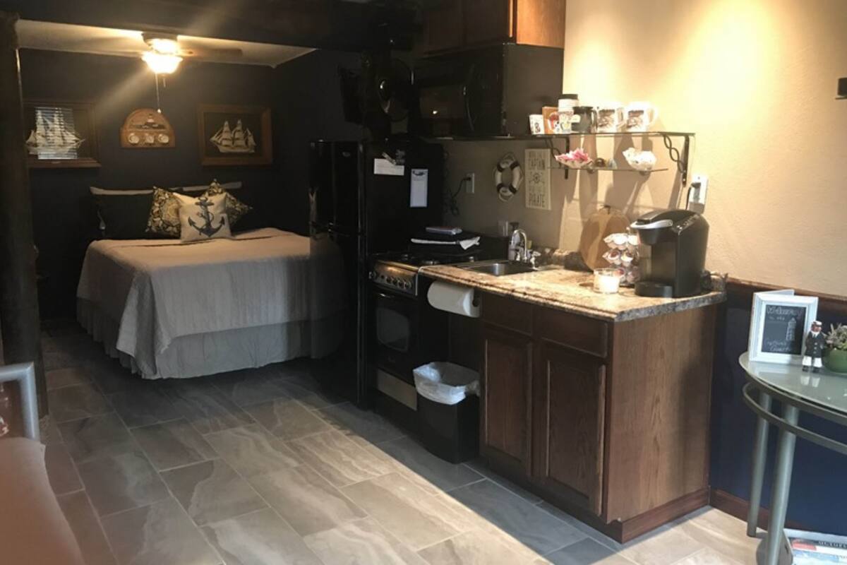 Een kleine slaapkamer met een bed, een klein kitchenette en een eethoek.