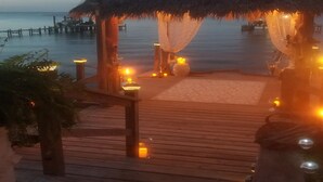 A wooden deck with a thatched-roof structure, candles, and a view of the sea.