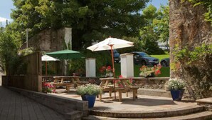 An outdoor patio area with wooden tables and benches, potted plants, and umbrellas. - Hotel Mariners (Haverfordwest)