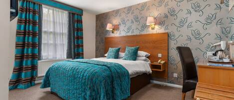 A hotel room with a large bed, a wooden headboard, two bedside lamps, a desk with a chair, and a radiator.