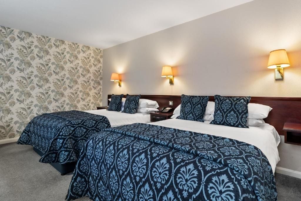 Een hotelkamer met twee bedden, behang met een patroon en wandlampen.