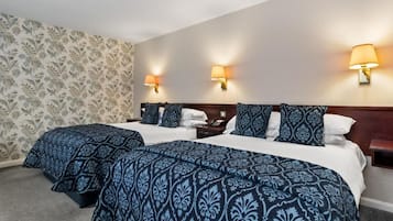 A hotel room with two beds, a patterned wallpaper, and wall-mounted lamps.