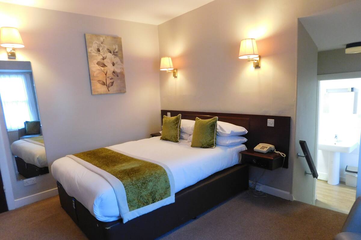 Ein Hotelzimmer mit einem großen Bett, zwei Nachttischlampen, einem Nachttisch, einem Telefon und einem Bild an der Wand.
