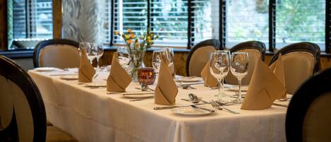 A dining table set with white tablecloth, napkins, and glassware, with chairs around it.
