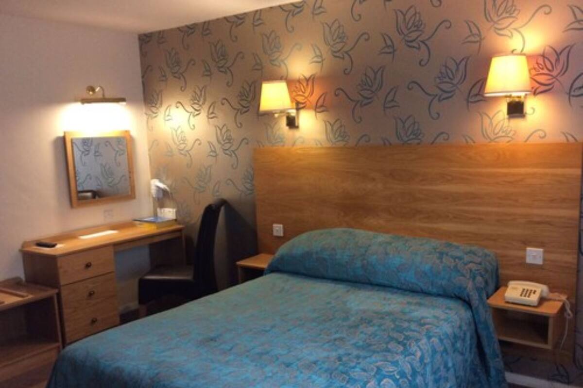 Ein Hotelzimmer mit einem Bett, einem Schreibtisch, einem Sessel, zwei Wandleuchten, einem Telefon und einem Spiegel.