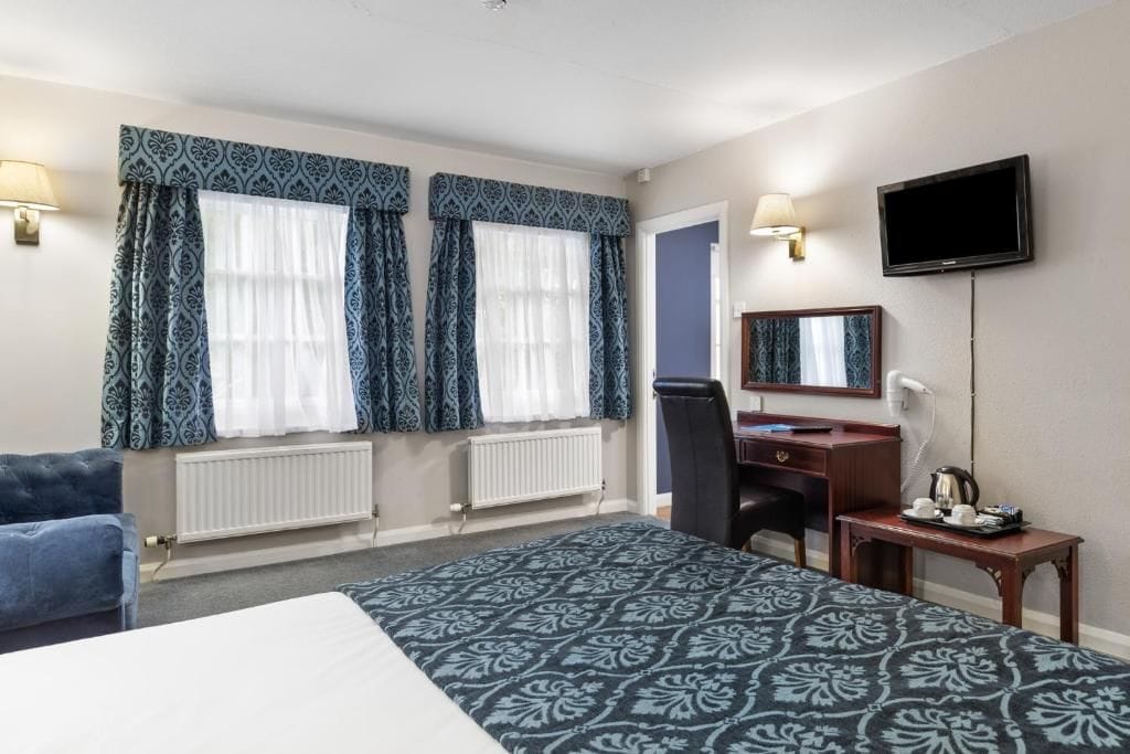 Ein Hotelzimmer mit Bett, Schreibtisch, Stuhl, Fernseher und einem Fenster mit Vorhängen.