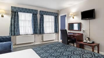 Ein Hotelzimmer mit Bett, Schreibtisch, Stuhl, Fernseher und einem Fenster mit Vorhängen.