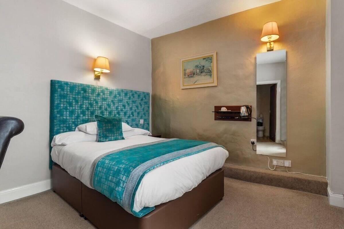 Ein Hotelzimmer mit einem Bett, zwei Wandleuchten, einem Gemälde, einem Spiegel und einem kleinen Ablagebrett mit Toilettenartikeln.