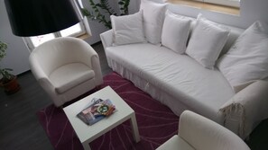 A living room with a white sofa, a white armchair, and a small white table with magazines. - The Art Quarter (Plovdiv)