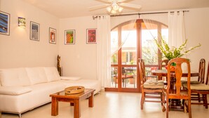 A living room with a white sofa, wooden coffee table, and a dining area with wooden chairs and a table.