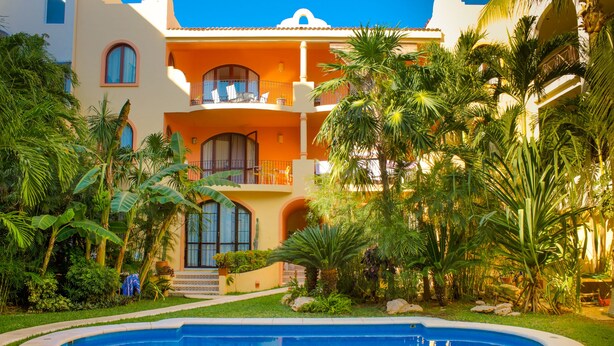 A hotel with a swimming pool, lush greenery, and a multi-story building with balconies.