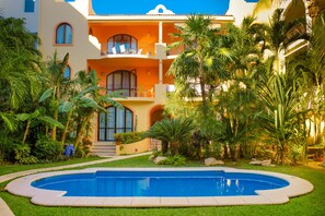 A hotel with a swimming pool, lush greenery, and a multi-story building with balconies. - Coccinella 301B by PRP (Playa del Carmen)