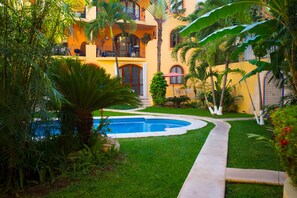 A pool surrounded by lush greenery and a yellow building with balconies.