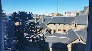 A view of a building with stone walls and multiple roofs, a tall antenna structure, and a tree in the foreground. - Civico Apartments (San Carlos de Bariloche)