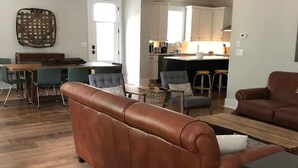 Un salon spacieux avec un canapé en cuir marron, une table basse en bois et un coin repas comprenant une table et des chaises en bois.