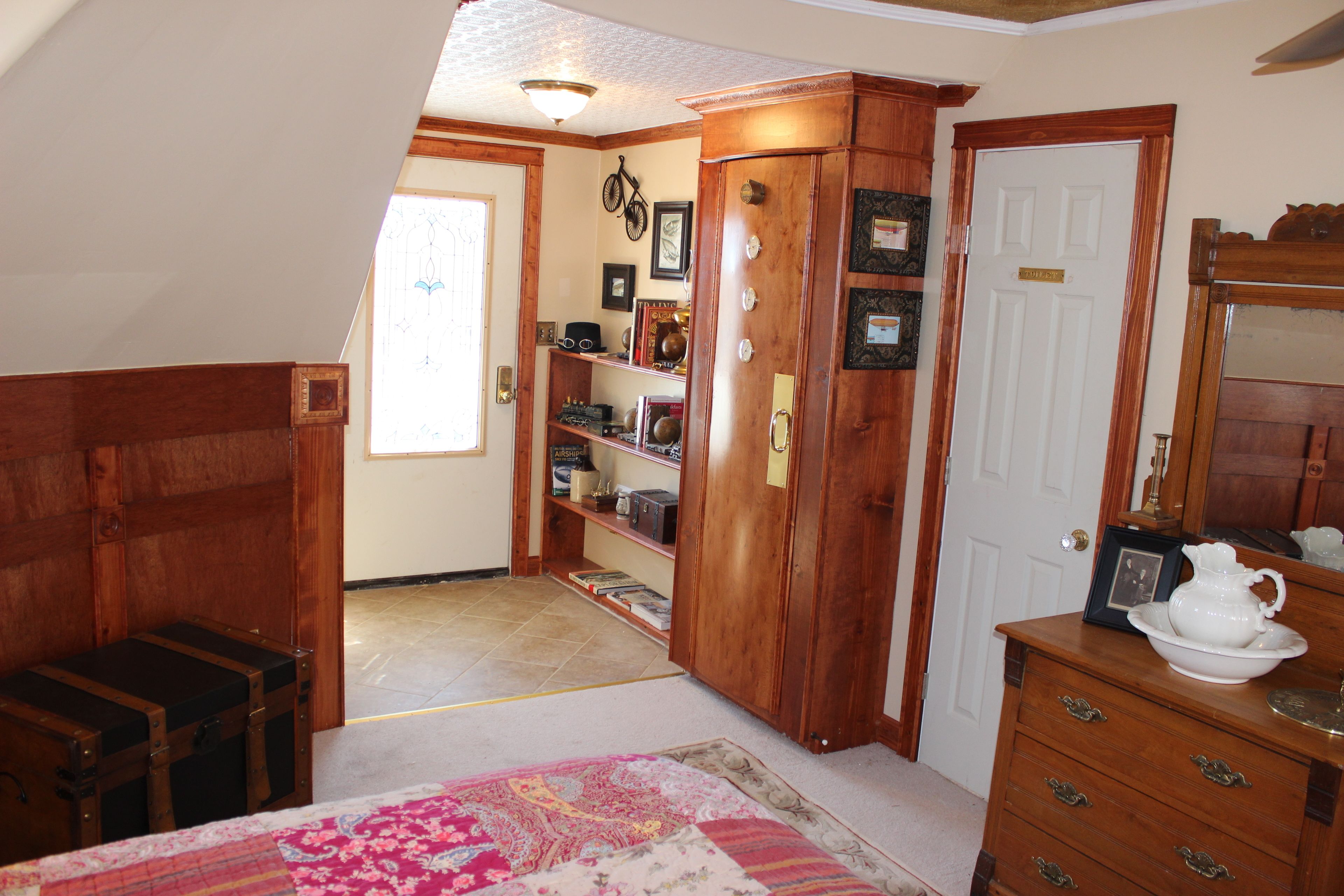 A room with a wooden cabinet, a white door, and a dresser with a white pitcher and bowl.
