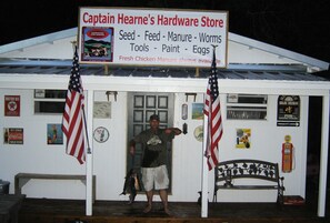 A hardware store with a signboard listing items like seed, feed, manure, worms, tools, paint, and eggs.