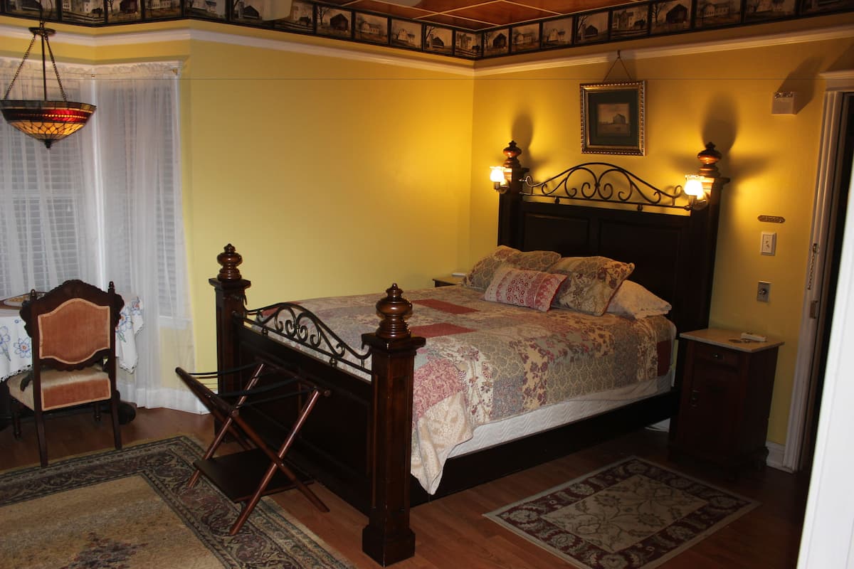 A bedroom with a wooden bed, a nightstand, a chair, and a hanging light fixture.