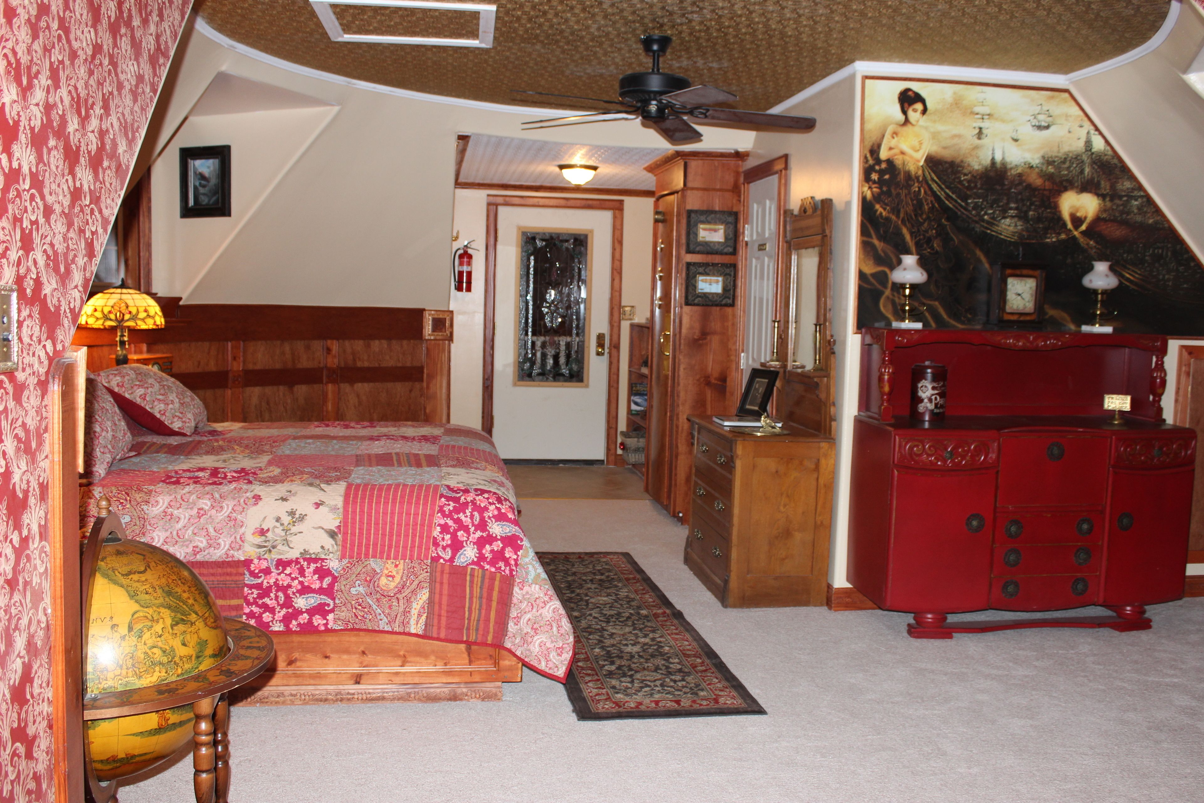 A bedroom with a bed, a dresser, a globe, and a painting.