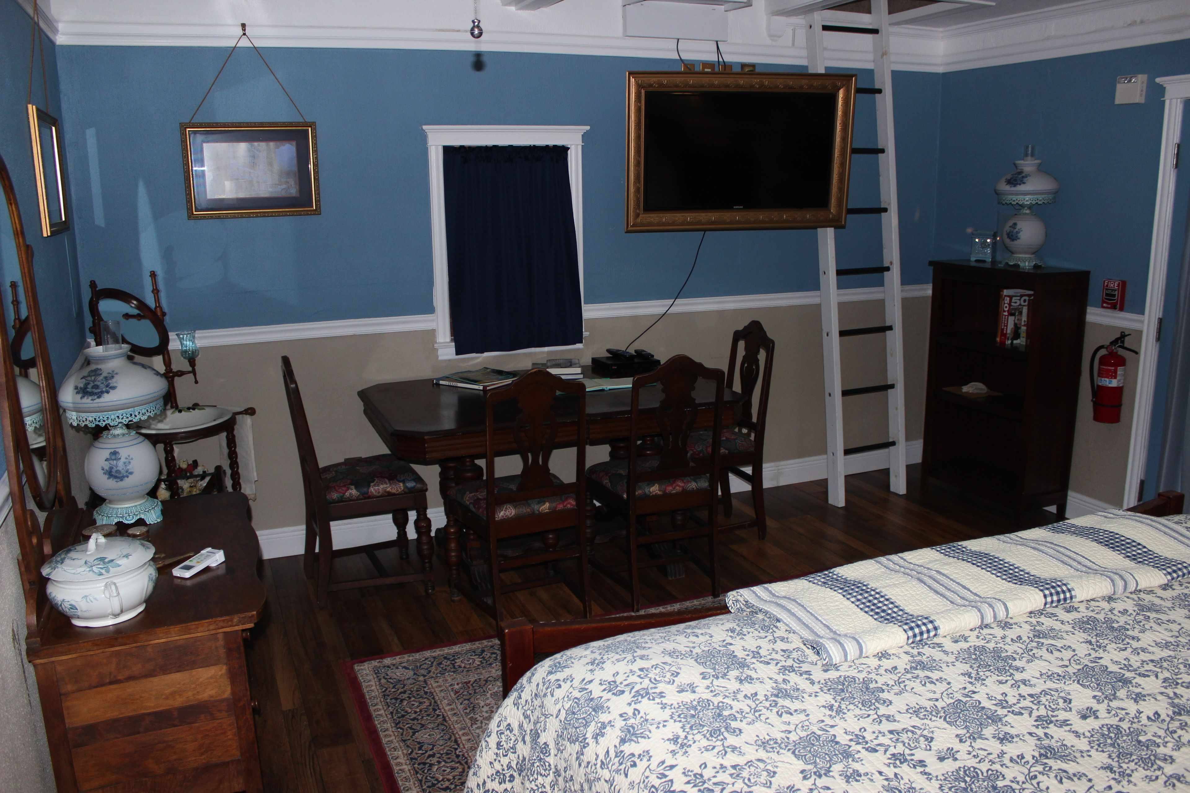 Una habitación con una cama, un escritorio con silla, un televisor montado en la pared y un armario.