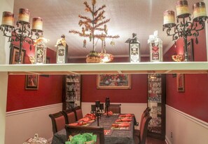 A dining area with a table set for four, a decorative tree, and a shelf with bottles and a candelabra.