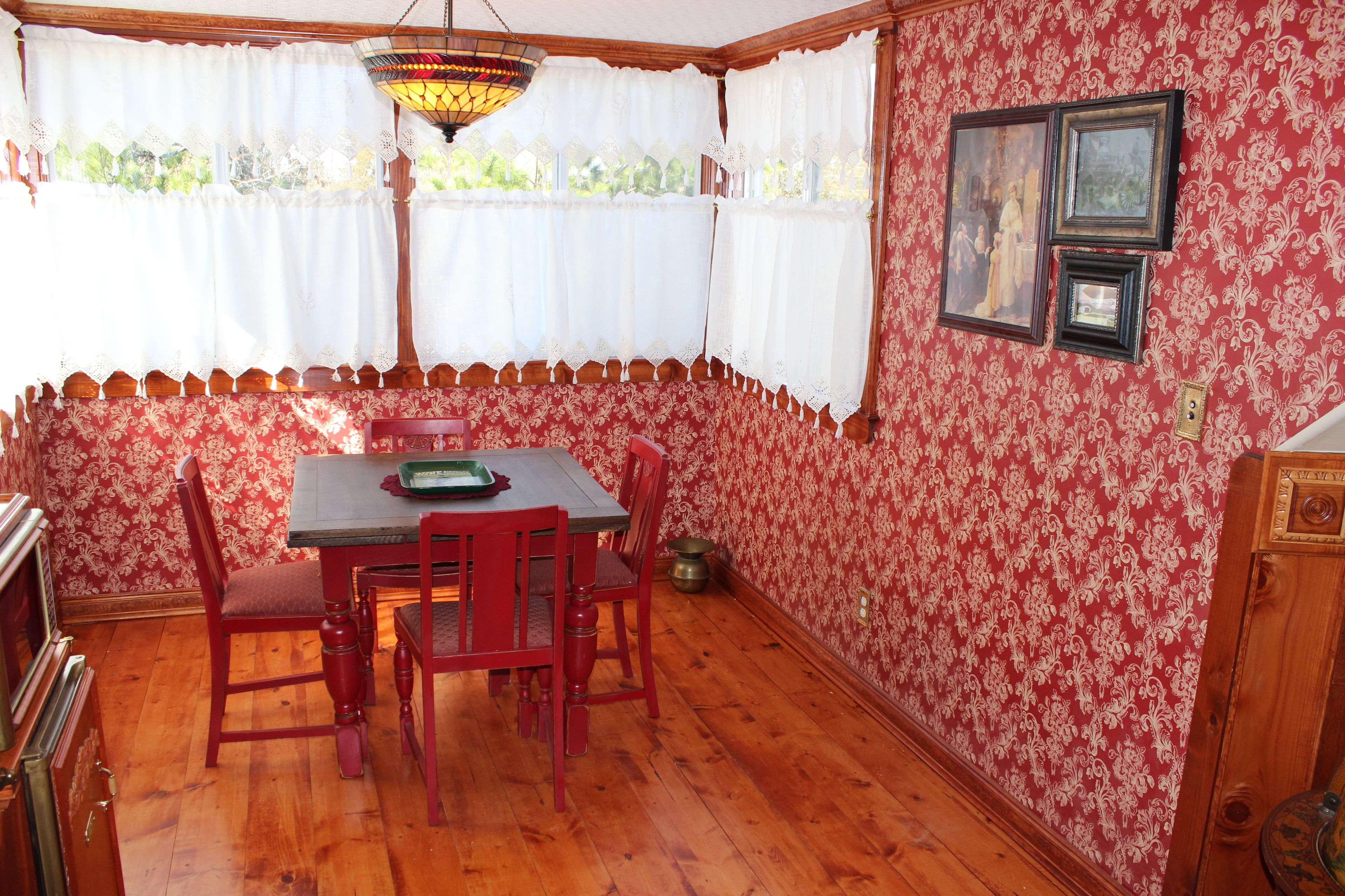 A dining area with a wooden table and chairs, a patterned wallpaper, and a window with white curtains.