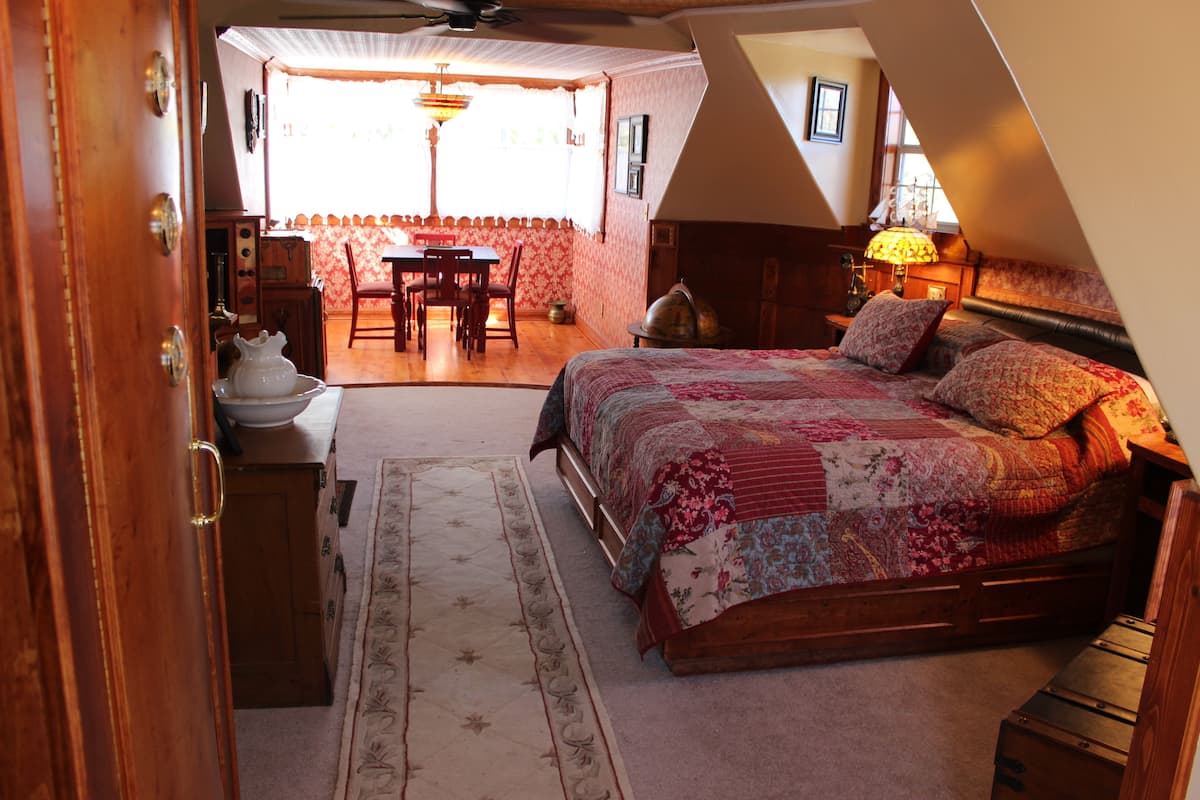 A bedroom with a large bed, a wooden dresser, a desk with chairs, and a dining area with a table and chairs.