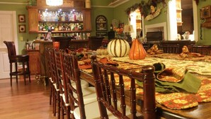 A dining area with a long wooden table, chairs, and a bar area with shelves of bottles. - Book Nook Inn (Lumberton)