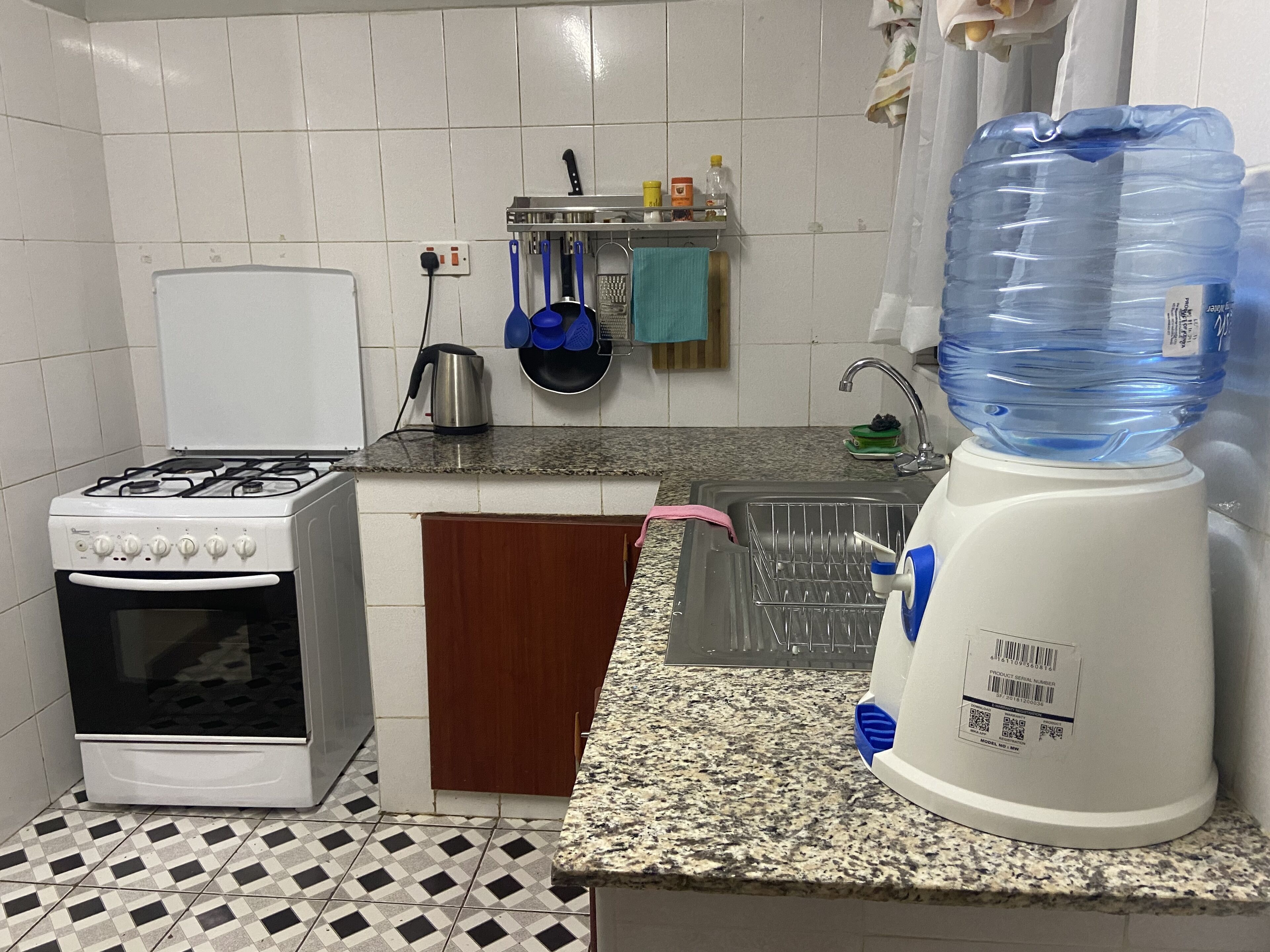 A kitchen with a gas stove, oven, granite countertop, sink, and a water dispenser.