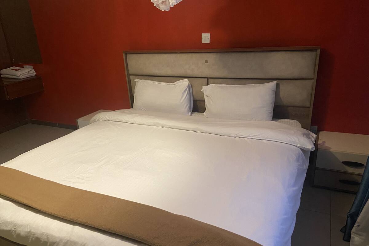 Hotelkamer met een bed, nachtkastje, lichtschakelaar aan de muur en een rode wand.