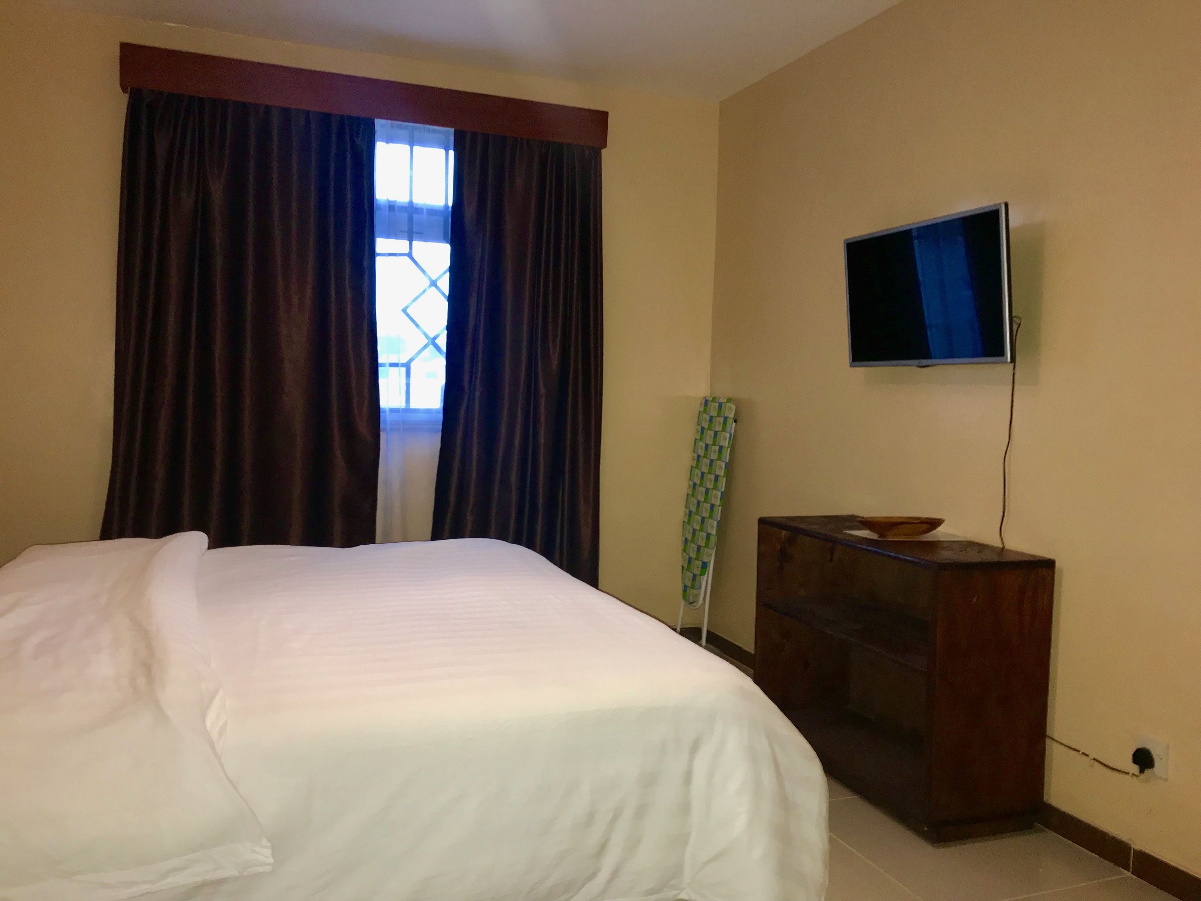 A hotel room with a bed, a television mounted on the wall, and a window with curtains.