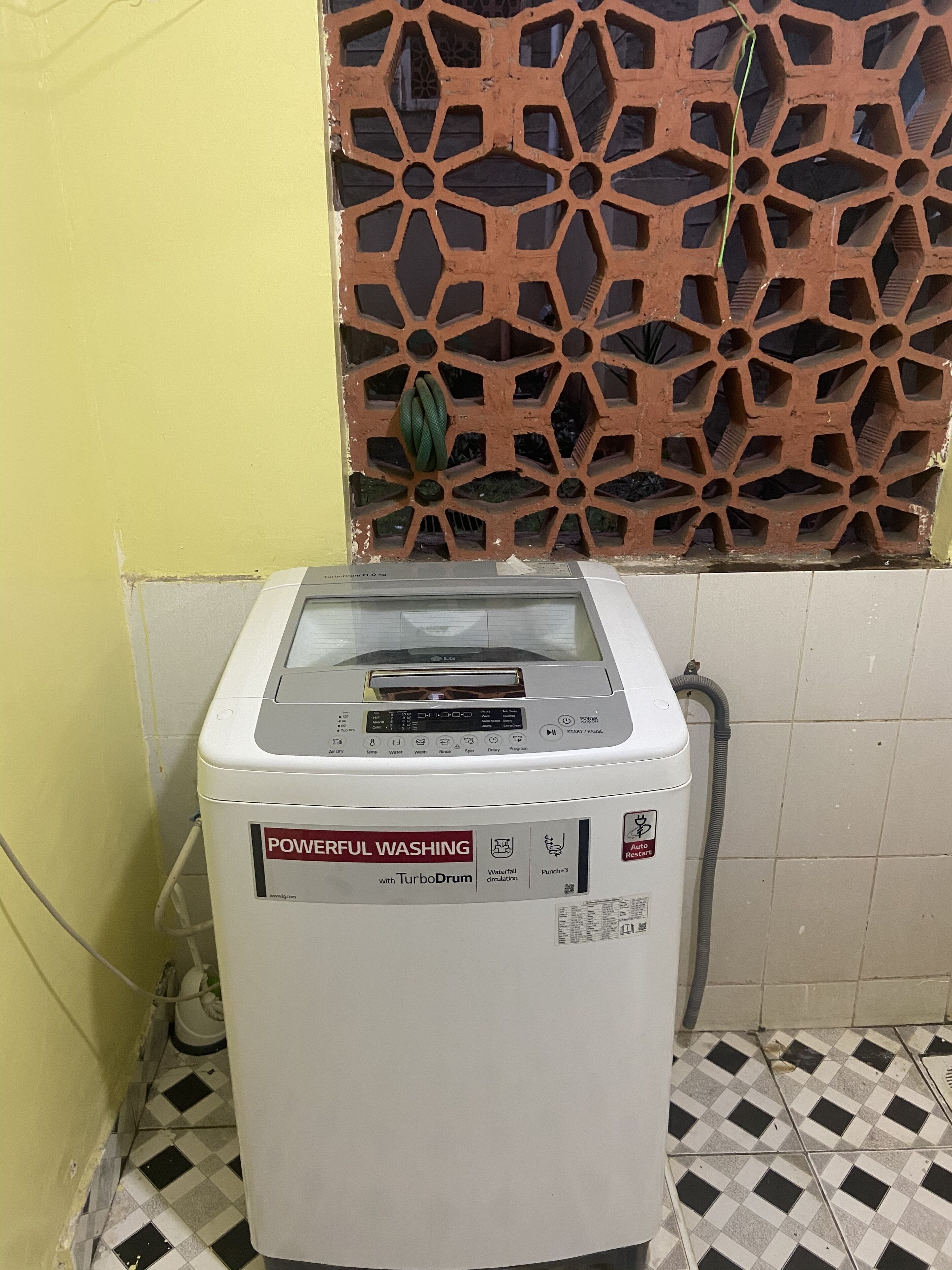 A washing machine with a digital display and multiple buttons, located in a room with a tiled floor and a decorative wall panel.