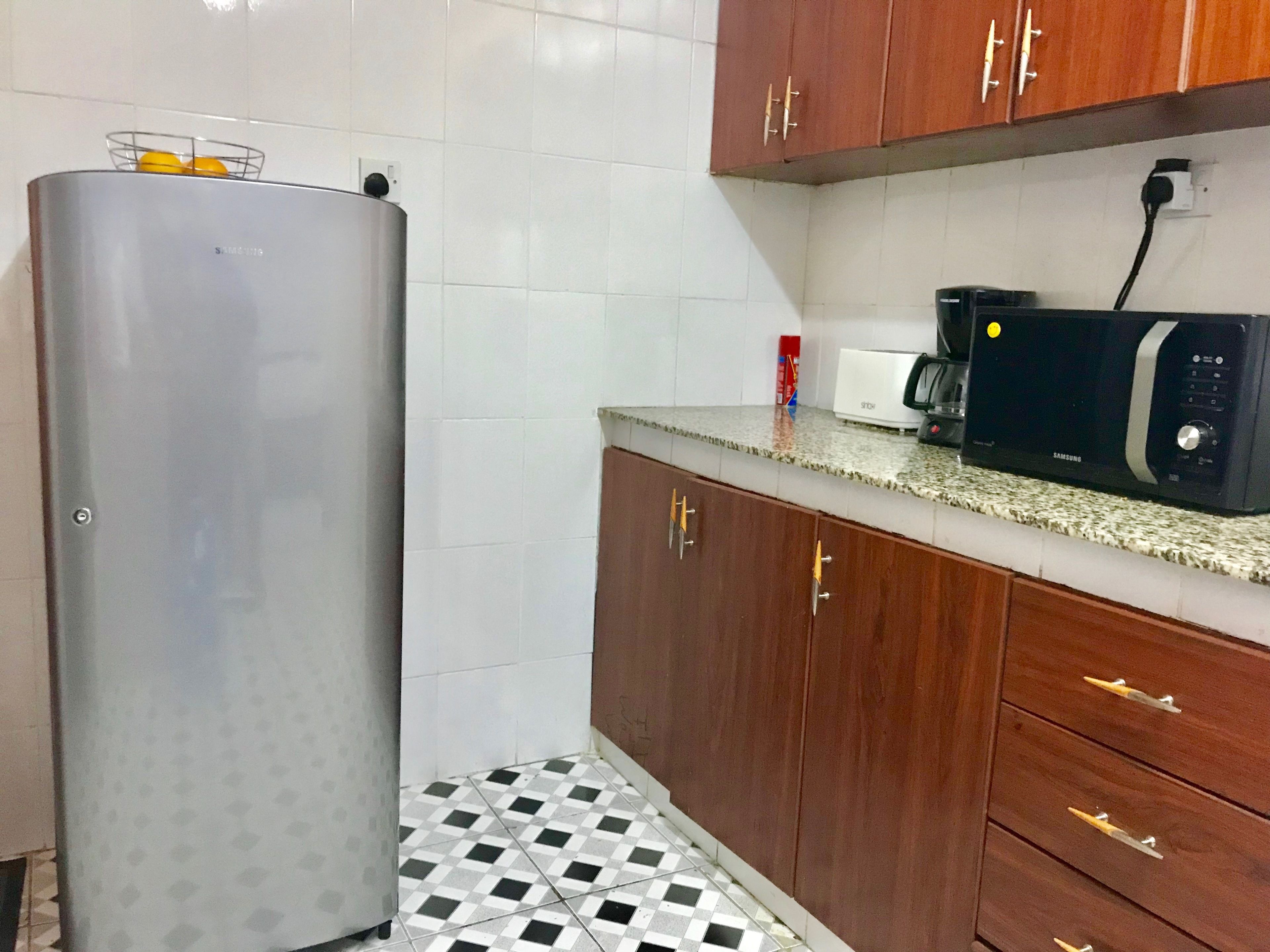 A kitchen with a refrigerator, microwave, coffee maker, and wooden cabinets.