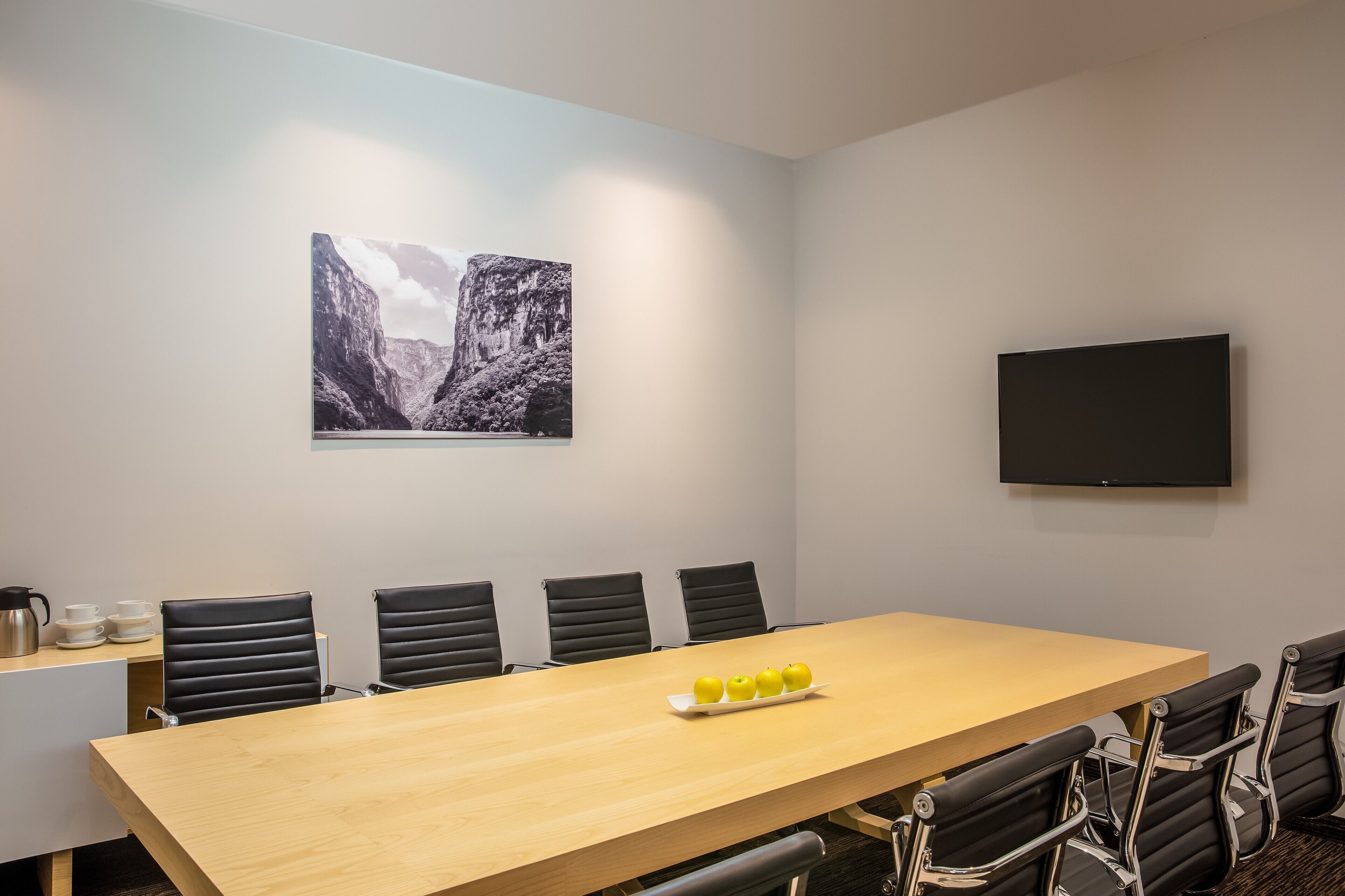 Una sala de conferencias con una mesa larga, seis sillas, un televisor de pantalla plana y un cuadro de un paisaje montañoso en la pared.