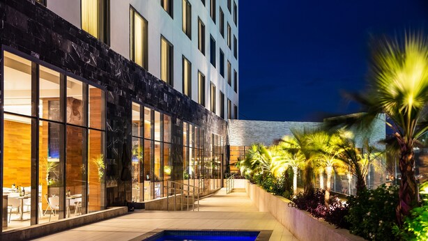 A modern hotel with a swimming pool, outdoor seating, and well-lit windows. - Fiesta Inn Tuxtla Fashion Mall (Tuxtla Gutierrez)