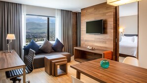 A modern hotel room with a large window, a flat-screen TV, a sofa with cushions, a wooden table, and a small seating area. - Fiesta Inn Tuxtla Fashion Mall (Tuxtla Gutierrez)