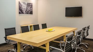 A conference room with a long table, six chairs, a flat-screen TV, and two framed pictures on the wall.