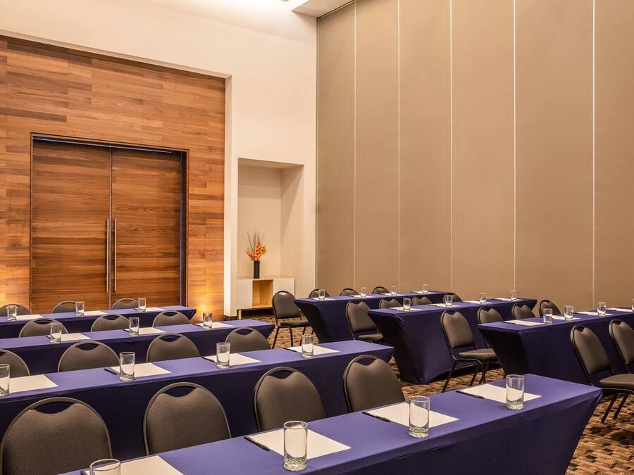A conference room with multiple tables and chairs, wooden panel walls, and a carpeted floor.