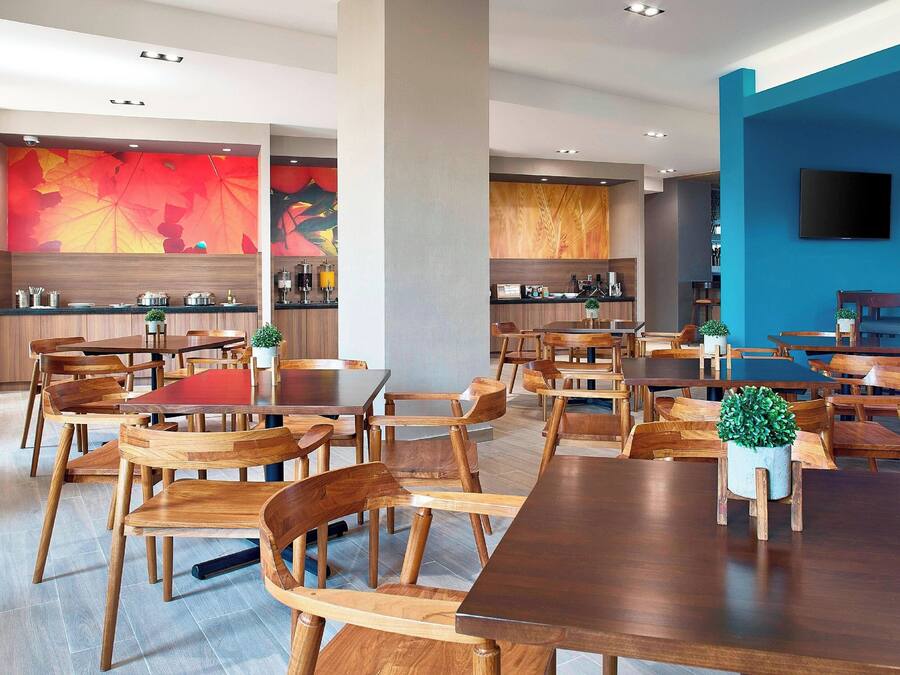 A modern dining area with wooden tables and chairs, a kitchen in the background, and a blue accent wall.