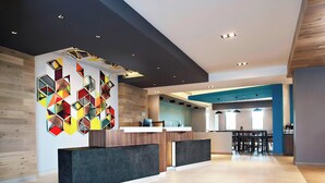 A modern reception area with a geometric wall art, a wooden reception desk, and a seating area with tables and chairs. - Fairfield Inn & Suites Aguascalientes (Aguascalientes)